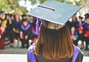 Woman standing in graduation attire facing colleagues.